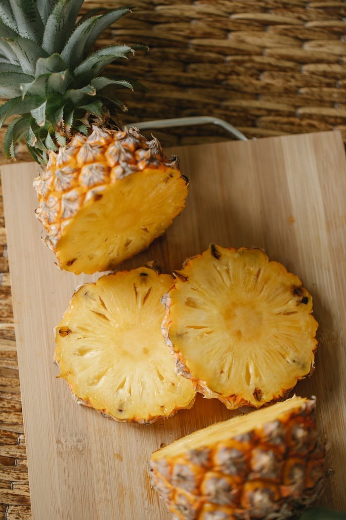 Top view halves of fresh exotic pineapple with green crown and round yellow pieces placed on cutting board in kitchen